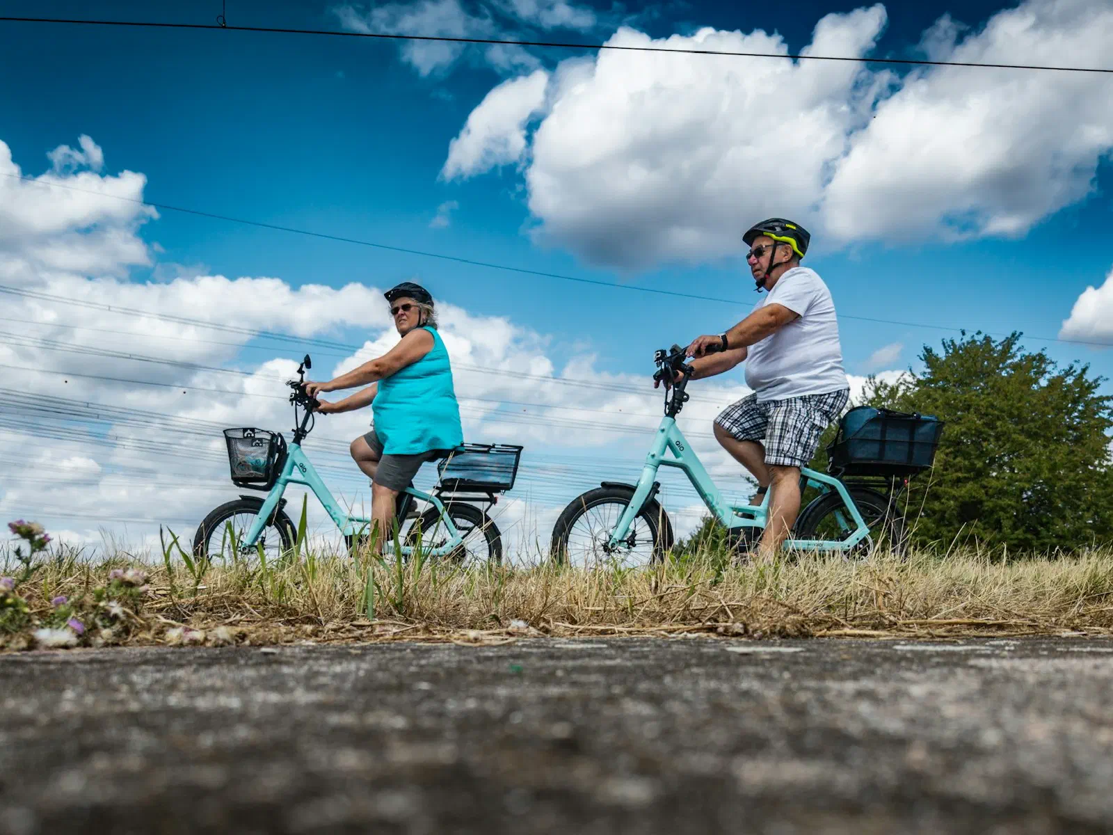 Un couple roule sur deux vélos bleu clair à cadre bas, sous un ciel nuageux.