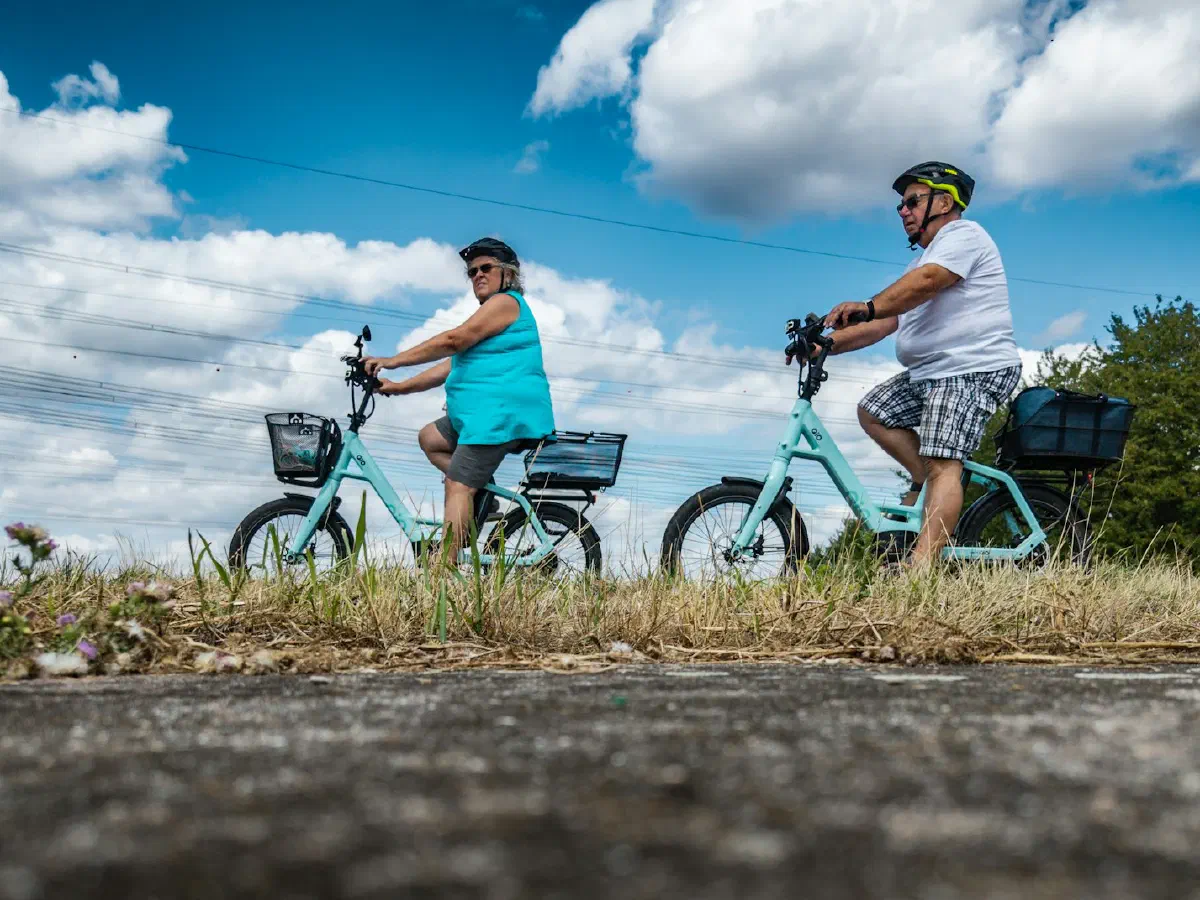 Un couple roule sur deux vélos bleu clair à cadre bas, sous un ciel nuageux.