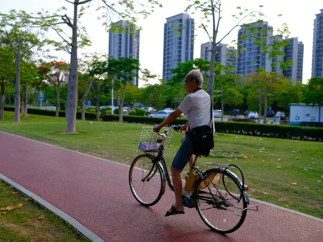 Un homme âgé roule sur un vélo de ville le long d'une piste cyclable rouge, des immeubles en arrière-plan.
