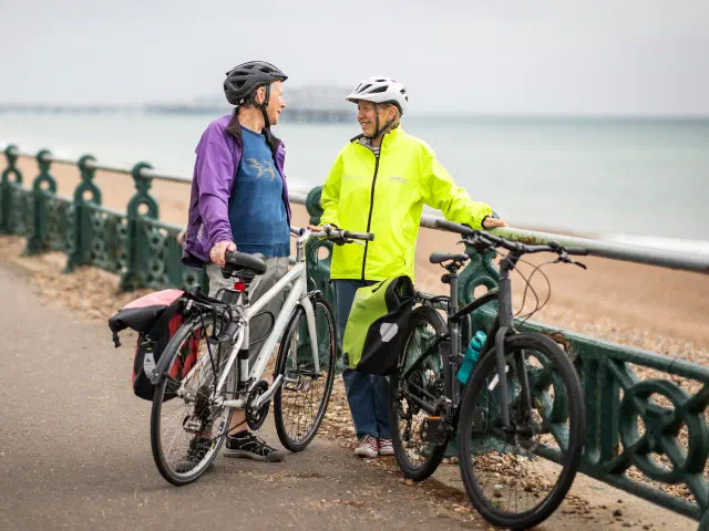 Deux cyclistes discutent à côté de leurs vélos sur une promenade en front de mer.