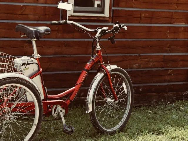Un tricycle adulte rouge avec panier, garé contre un mur en planches.