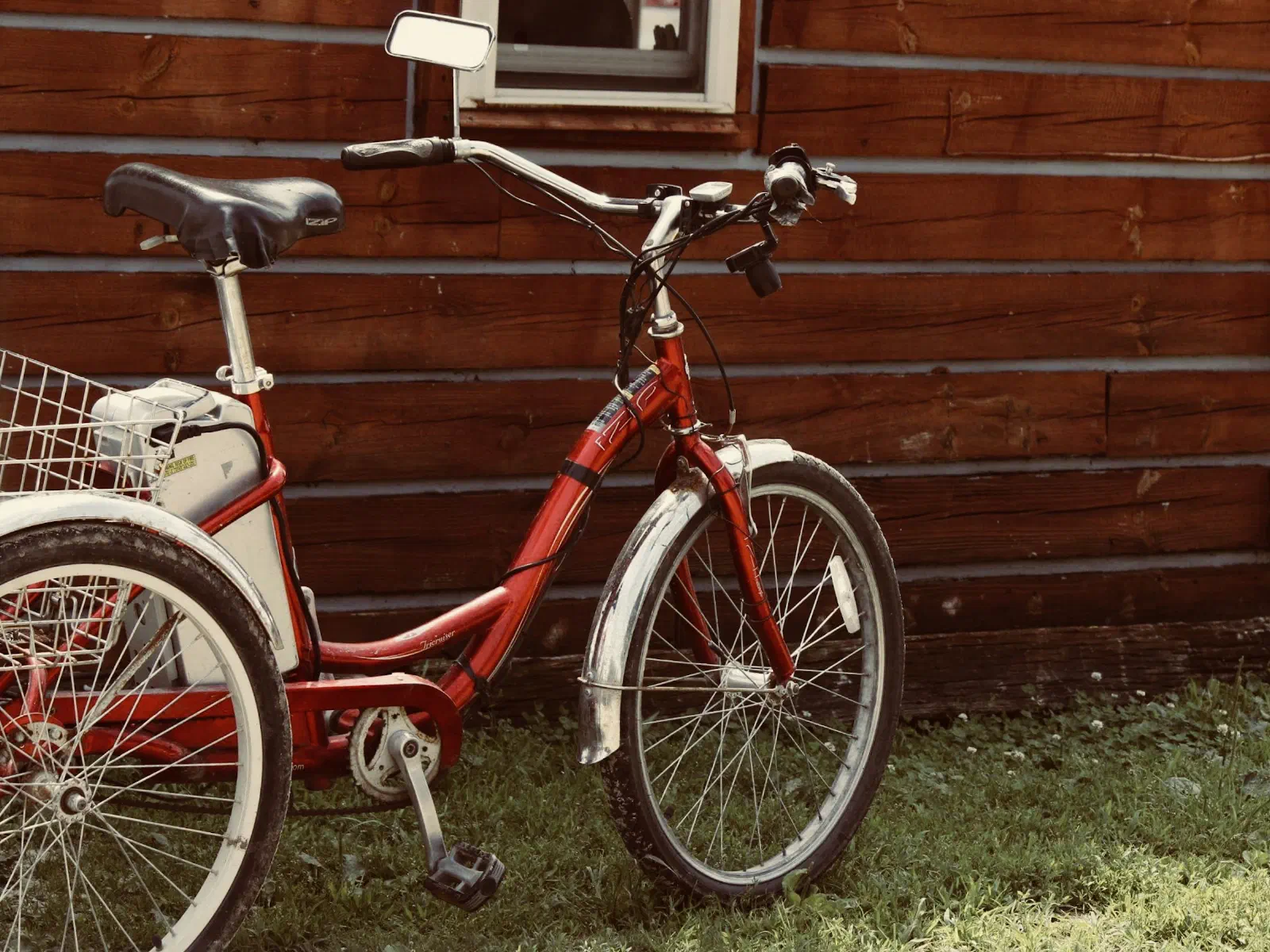 Un tricycle adulte rouge avec panier, garé contre un mur en planches.