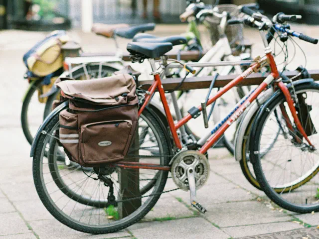 Un vélo de ville rouge avec une sacoche de porte-bagages en cuir, attaché à un arceau sur un trottoir.
